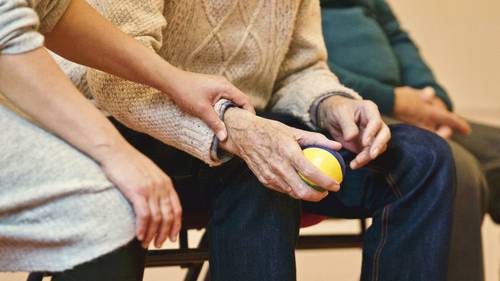 Nahaufnahme einer alten Hand die einen Ball hält, eine jüngere Hand liegt helfend am Handgelenkt