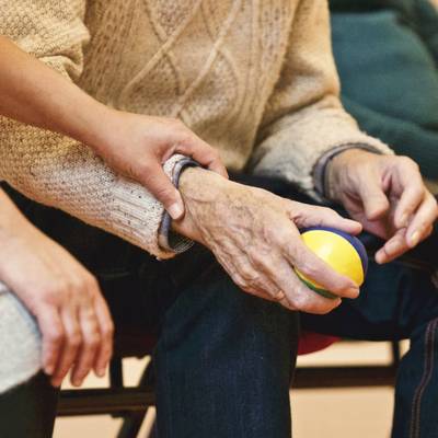 Nahaufnahme einer alten Hand die einen Ball hält, eine jüngere Hand liegt helfend am Handgelenkt