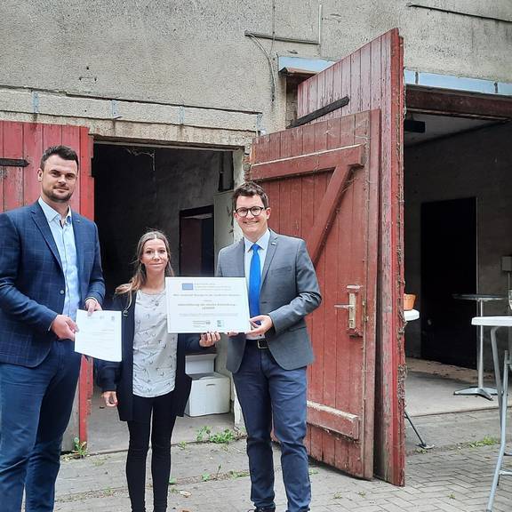 Landrat Tino Schomann und Anja Witt vom StALU Westmecklenburg überreichten die Förderung und die Förderplakette an den Bürgermeister von Boltenhagen Raphael Wardecki.