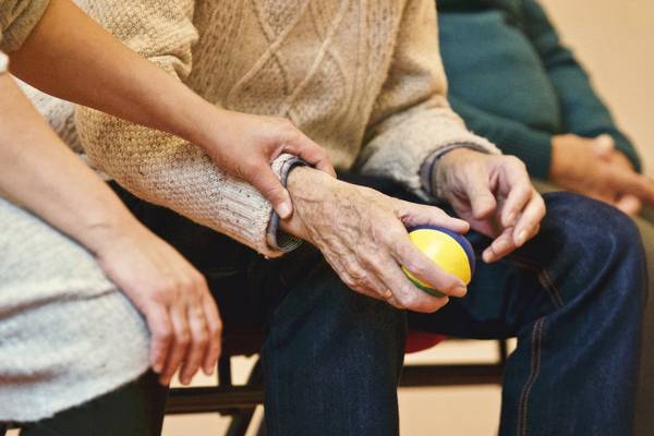 Nahaufnahme einer alten Hand die einen Ball hält, eine jüngere Hand liegt helfend am Handgelenkt