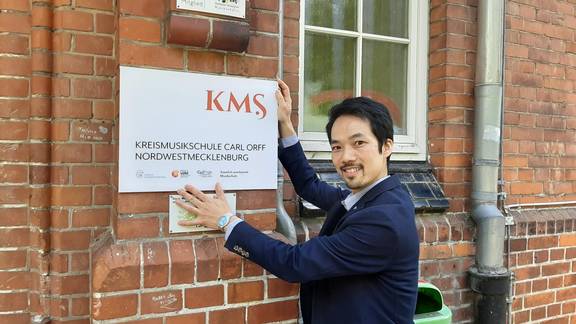 KMS-Direktor Hidehisa Edane zeigt, wo das neue Logo an der Kreismusikschule in Wismar hängen wird.