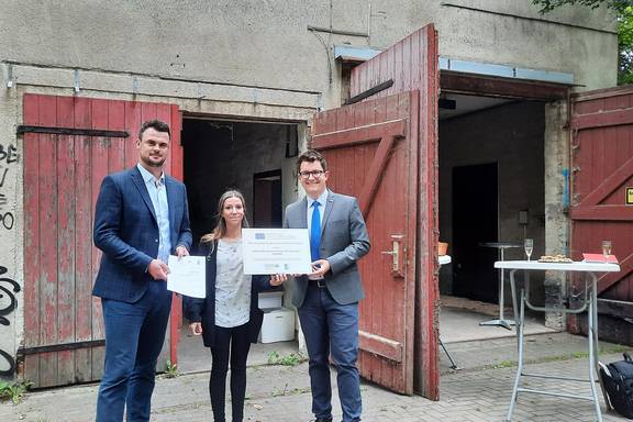 Landrat Tino Schomann und Anja Witt vom StALU Westmecklenburg überreichten die Förderung und die Förderplakette an den Bürgermeister von Boltenhagen Raphael Wardecki.